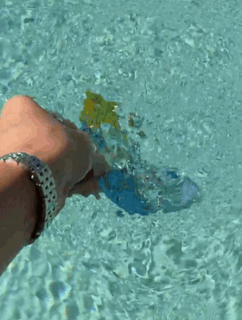 Hand wearing a watch twirls a colorful bucket underwater, creating splashes