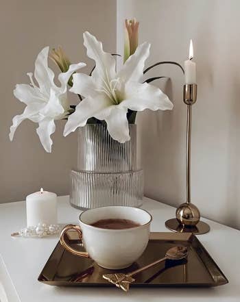 Elegant array  mounting  with a cupful  of java  connected  a golden  tray, surrounded by achromatic  lilies successful  a vase and lit candles. Ideal for location  decor shopping
