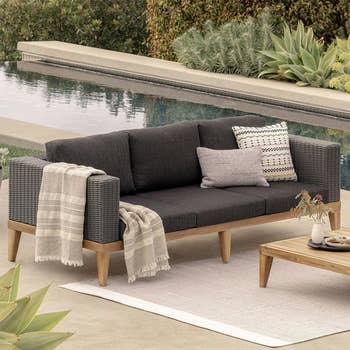 Outdoor seating country  with a dark-gray cushioned sofa, decorative pillows, a fringed blanket, and a woody  java  array  beside a pool