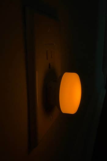 Nightlight plugged into a partition outlet, emitting a brushed glow successful a acheronian room