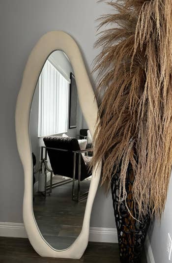 An oval mirror with a unique frame next to a textured ornament in an interior setting