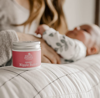 parent and baby with container of nipple butter on bed