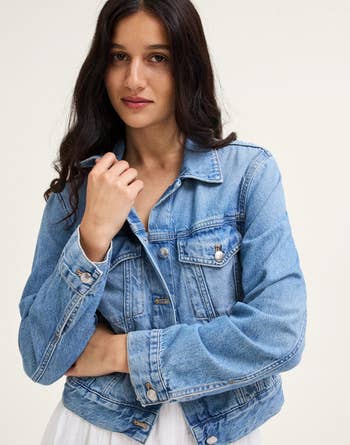 A person wearing a stylish denim jacket over a light dress, showcasing a casual yet chic look