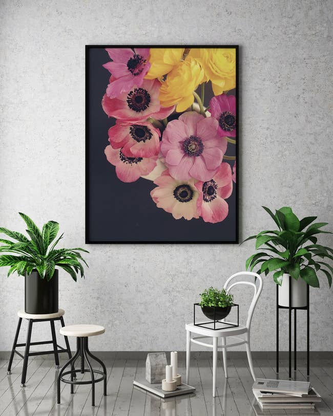 Large framed floral artwork on a wall above a modern indoor plant setup with various stands and pots