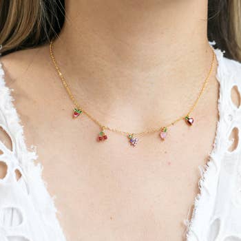 a model wearing a gold necklace with five fruit charms on it