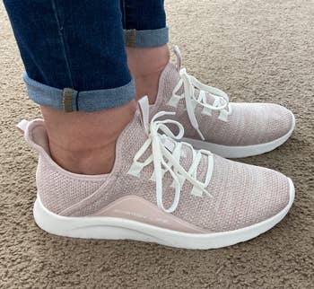 Person wearing light pink slip-on sneakers with laces and cuffed jean