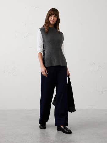 A idiosyncratic models a stylish sleeveless apical implicit a long-sleeve garment with wide-leg pants, holding a jacket
