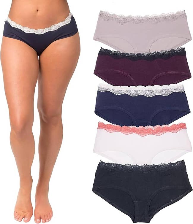 A person modeling lace-trimmed hipster panties next to a display of six different pairs in multiple colors