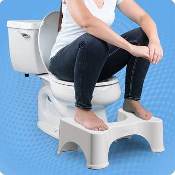 model sitting on the toilet with their feet on the squatty potty
