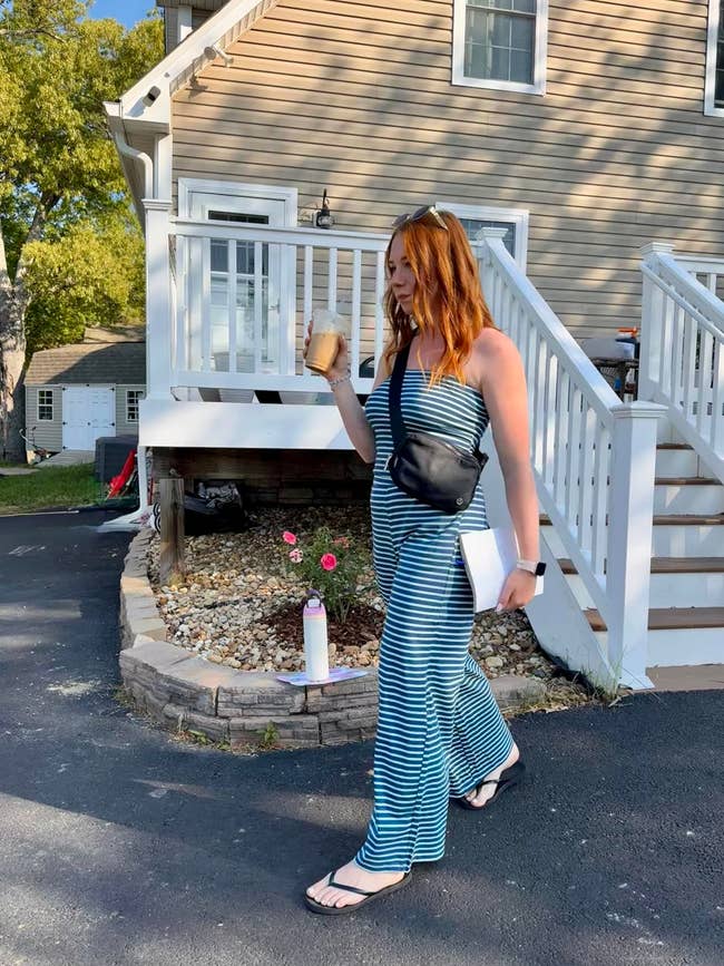 Woman successful  striped jumpsuit and flip-flops holds a portion  and notebook, walking extracurricular  a house