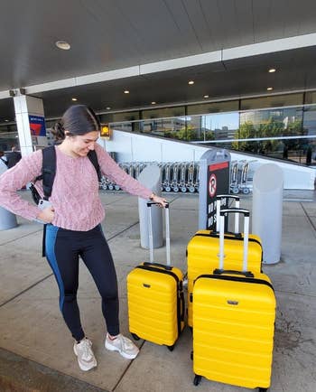 a reviewer standing next to three yellow suitcases of different sizes