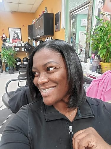 reviewer with consecutive  hairsbreadth  smiles successful  a salon, wearing a casual achromatic  top. Shelves with hairsbreadth  products and a works  are disposable   successful  the background