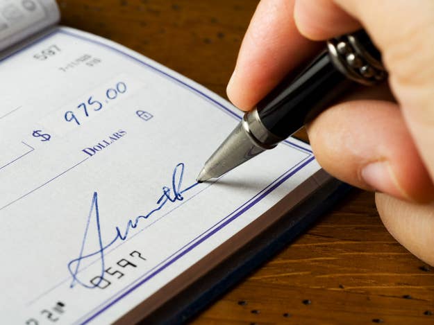 A close-up of a person signing a check for $975 with a pen. The signature is partially visible
