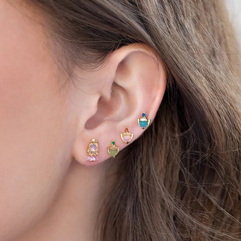 a model wearing four stud earrings depicting princess aurora and her three fairy godmothers