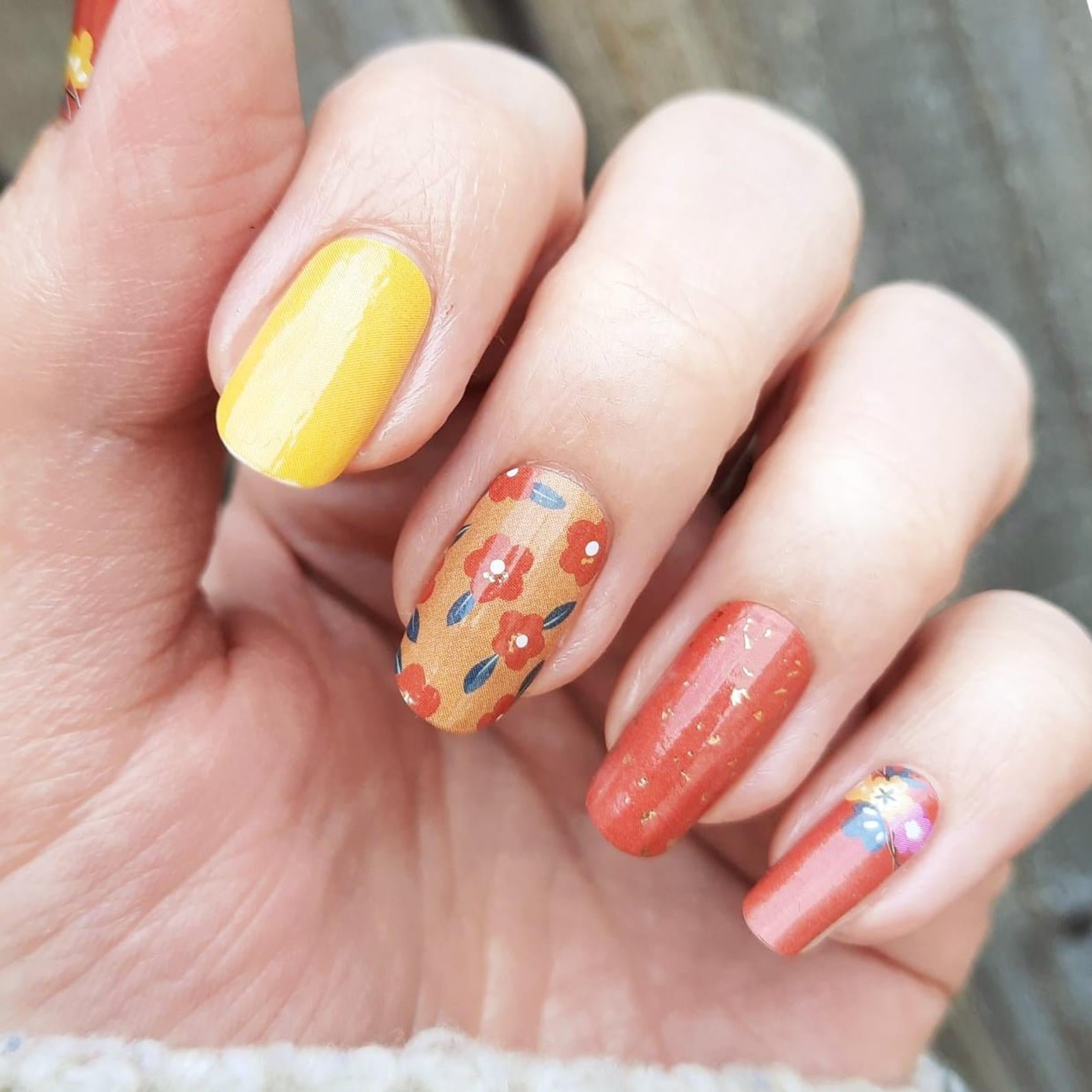 hand wearing nail wraps with a 70s mod style, like orange flowers, yellow, and deep orange