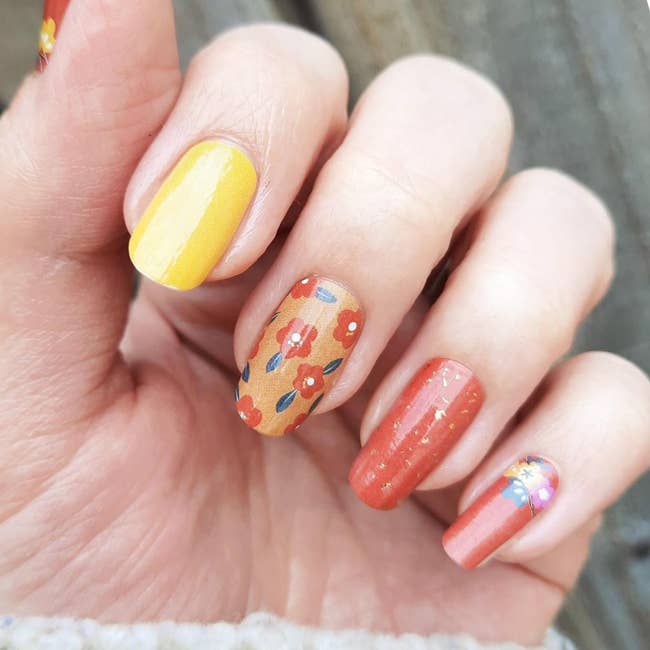 hand wearing nail wraps with a 70s mod style, like orange flowers, yellow, and deep orange