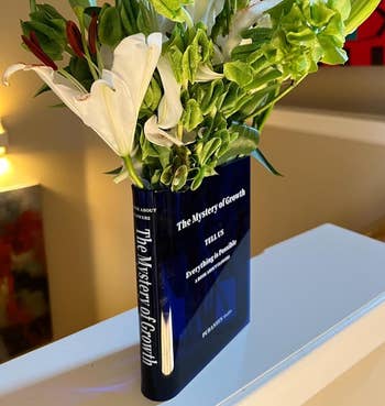navy transparent book-shaped vase with flowers in it
