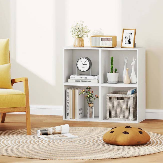 Living room scene with a white cube shelf displaying decorative items, books, and plants. A round rug and yellow chair complete the cozy setup