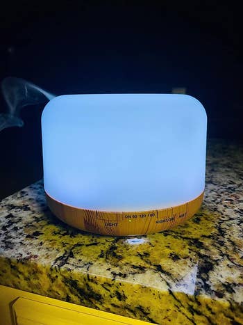 Diffuser emitting steam, set on a counter with a wood trim and light indicators