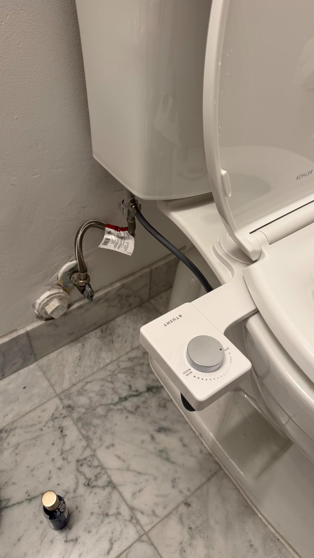 Toilet with a bidet attachment and a vessel  connected  the marble floor, showcasing bath  upgrade options