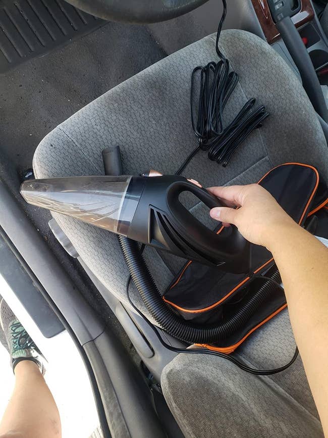 reviewer holding black small car vacuum above gray car seat