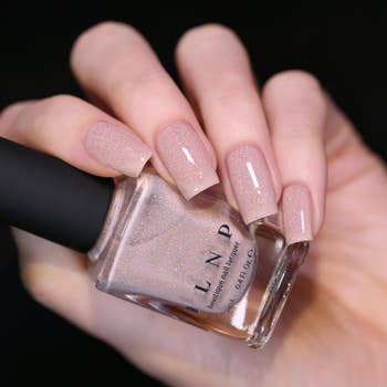 A hand with a lighter skin tone and square shaped nails painted with polish holding the bottle 