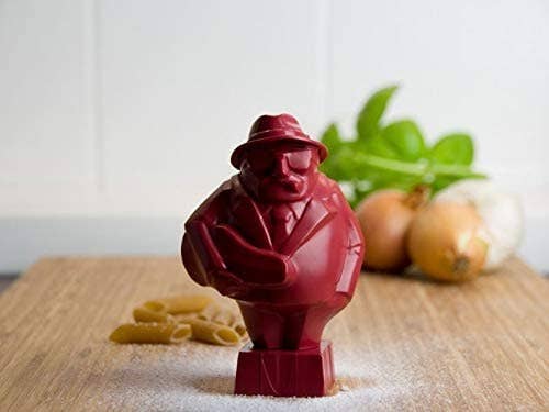 a man-shaped red figure standing on a cutting board next to some pasta 