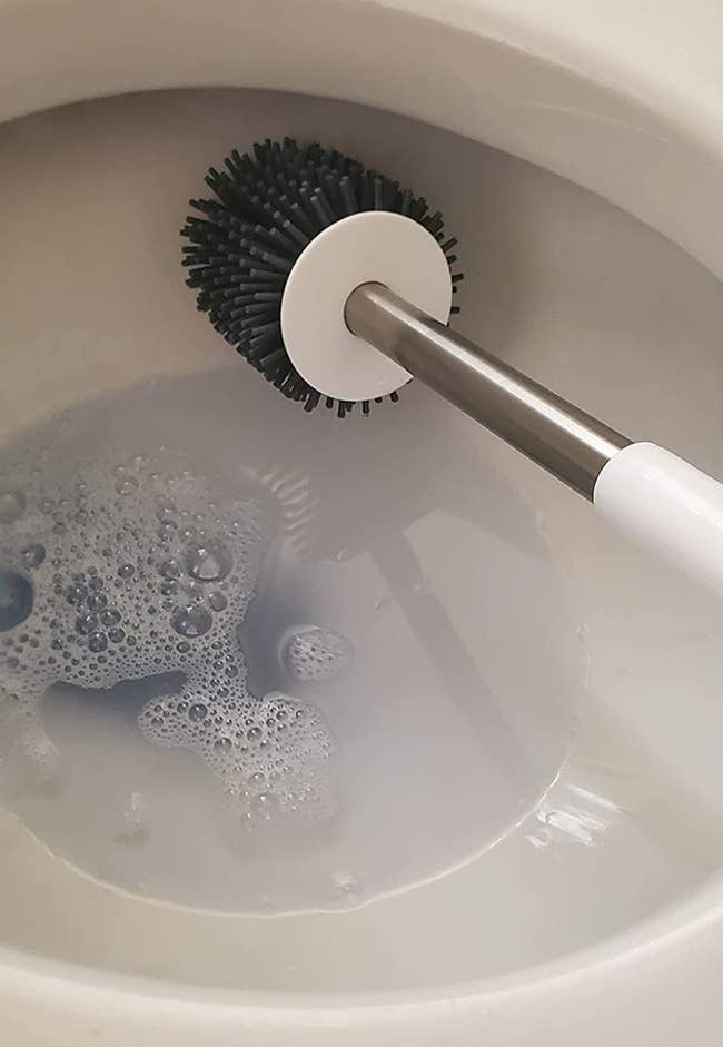 Reviewer using a gray silicone bristle brush to clean out a toilet 