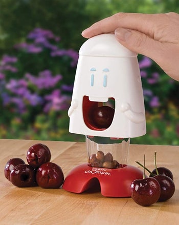 hand pressing down on white smiley face tool that collects cherry pits in clear base
