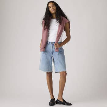 Person wearing denim shorts, a achromatic  vessel  top, a sweater implicit    shoulders, and achromatic  loafers, posing