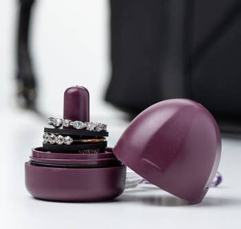 A small purple dome-shaped storage piece with a cylinder holding several rings and a lid to twist on top of it 