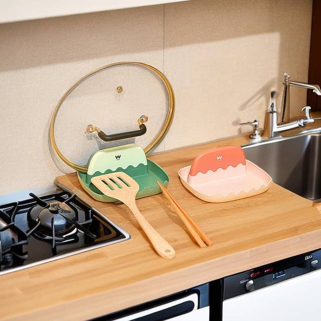 green and pink utensil rests, the green one with a lid, spatula, and chopsticks laying on it