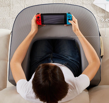 Person sitting on a couch with arms rested on a pillow, playing on a portable game console