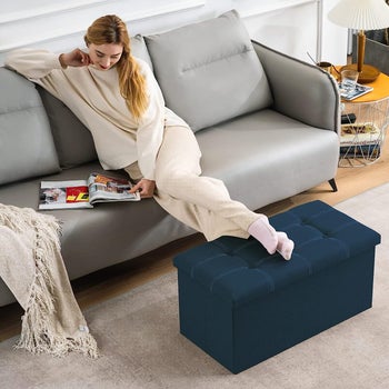 Model resting their feet on the storage ottoman in blue with the lid closed