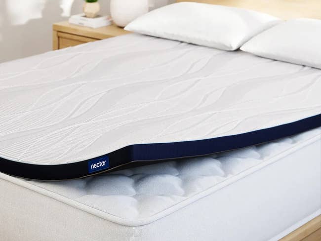 A representation  foam mattress topper connected  a furniture  with pillows, featuring a wavy signifier   and a branded edge