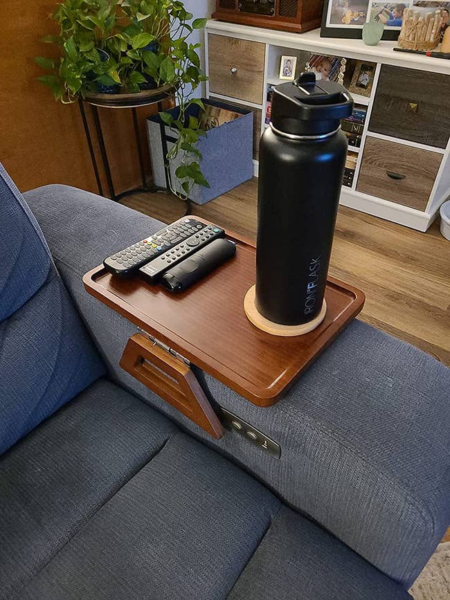 wood couch tray holding remotes and black tumbler on gray couch arm