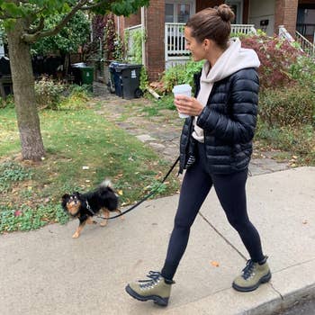 model in casual attire walks a small dog while wearing the sage boots