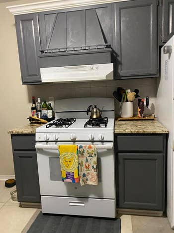 A reviewer's after photo with A tidy kitchen corner with a gas stove, range hood, and side refrigerator, featuring decorative towels on the oven handle