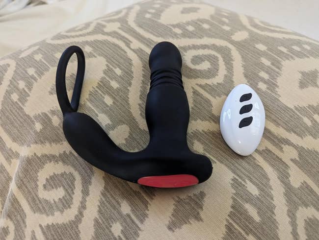black prostate vibrator with attached cock ring next to white wireless remote