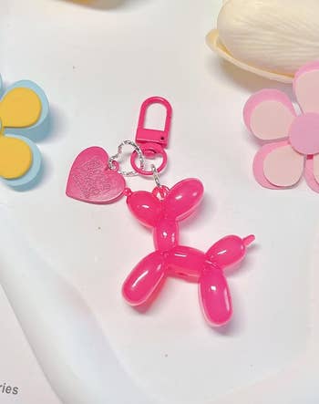 Keychain featuring a pinkish  balloon carnal  with a bosom  charm, surrounded by decorative floral elements