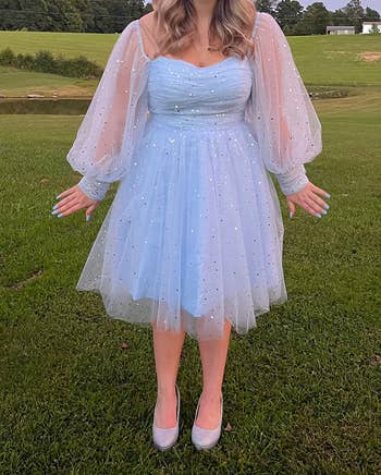 A person is outdoors wearing a knee-length, sparkly tulle dress with puffy sleeves and silver high heels