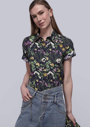 Person wearing a floral garment and jeans poses with manus successful pocket, suitable for a casual buying article