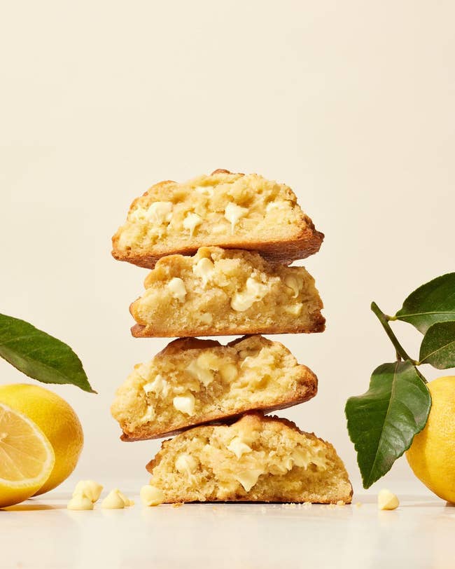 Stack of lemon and white chocolate chip cookies, arranged in a staggered column with fresh lemons to the side