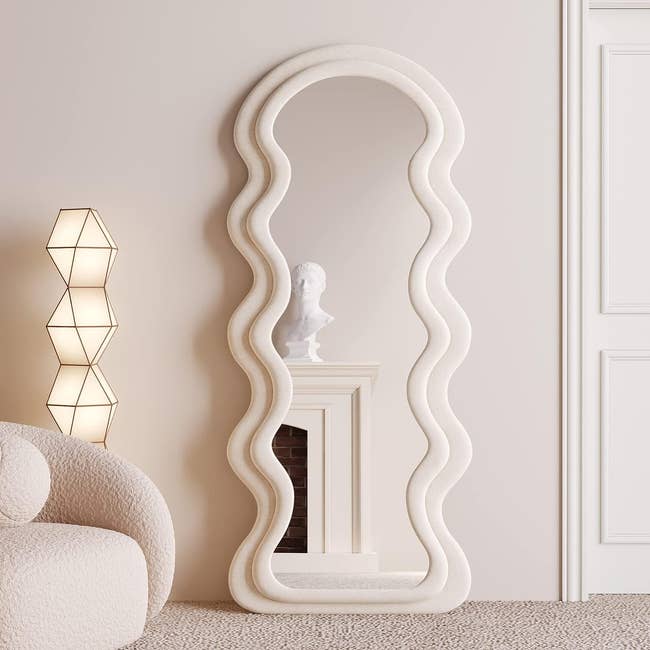 the wavy white mirror resting on the floor