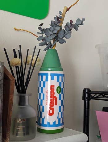 A vintage style green crayon shaped vase with flowers coming out of it on a nightstand 