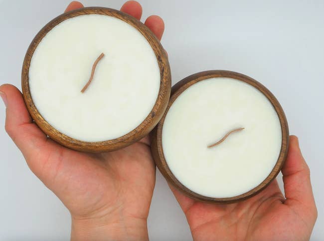 two hands each holding a candle in an acacia bowl