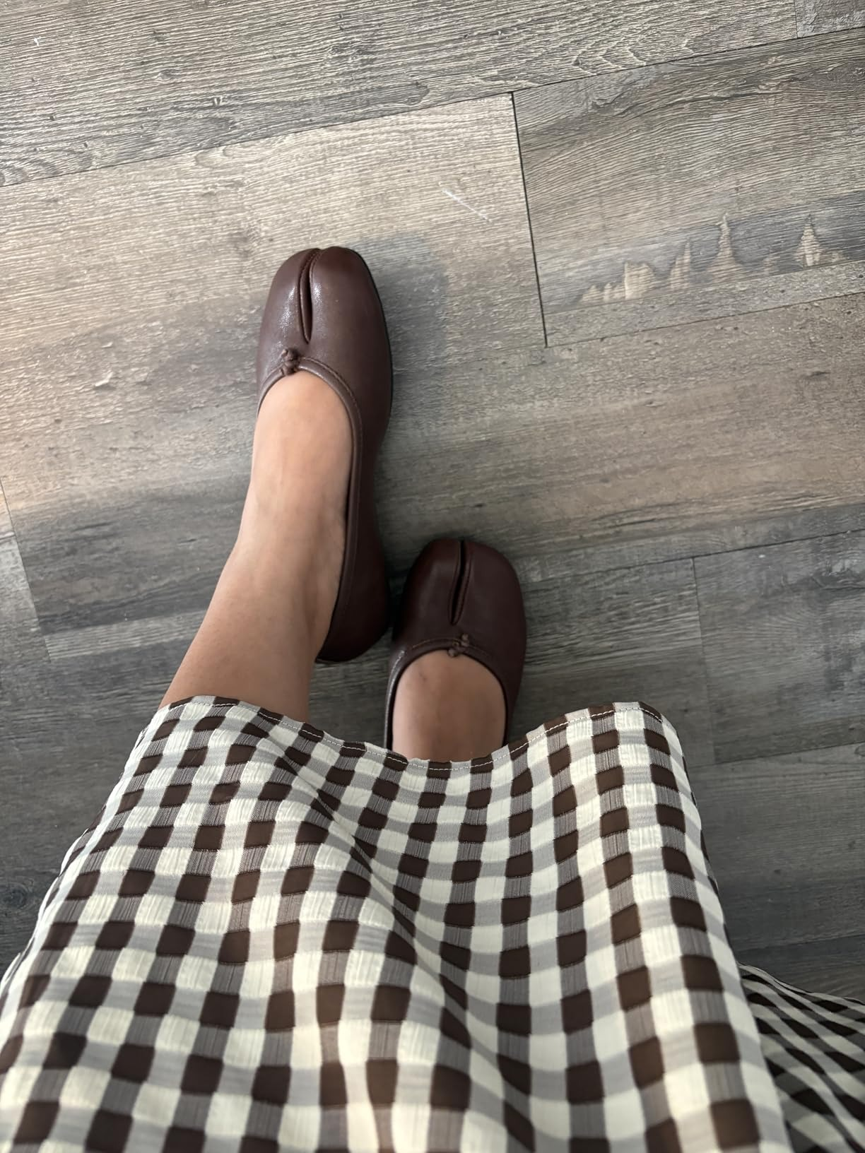 Person wearing brown, split-toe shoes with a checkered skirt lasting  connected  a woody  floor