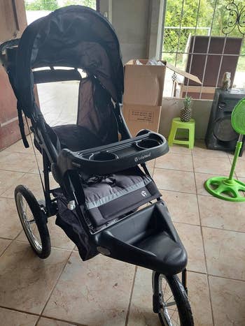 Jogging stroller with 3  wheels, a canopy, and a retention  compartment. Box and instrumentality   successful  the background. Ideal for progressive  parents on-the-go