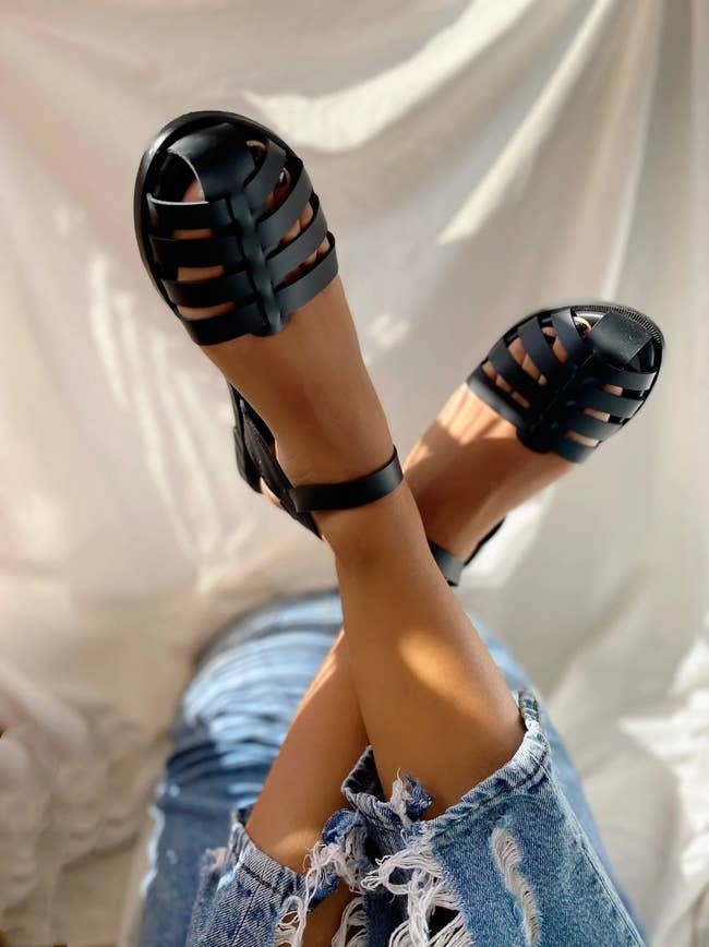 Model lying down, wearing black leather sandals and jeans