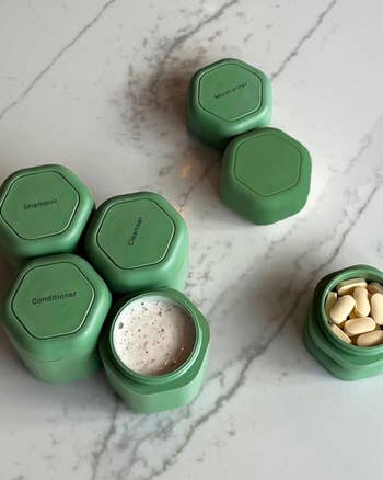 Hexagon-shaped green containers labeled shampoo, conditioner, and supplements on marble surface